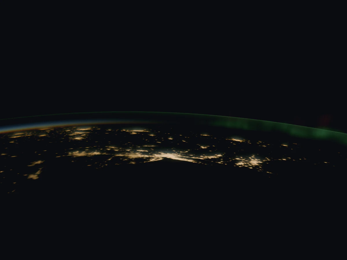 Night over eastern North America seen from orbit: city lights below, a band of sunset along the curve of the Earth, a thin green line of airglow above it and aurora to the north.